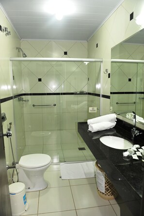A modern bathroom with a glass-enclosed shower, a black countertop sink, and a white toilet.