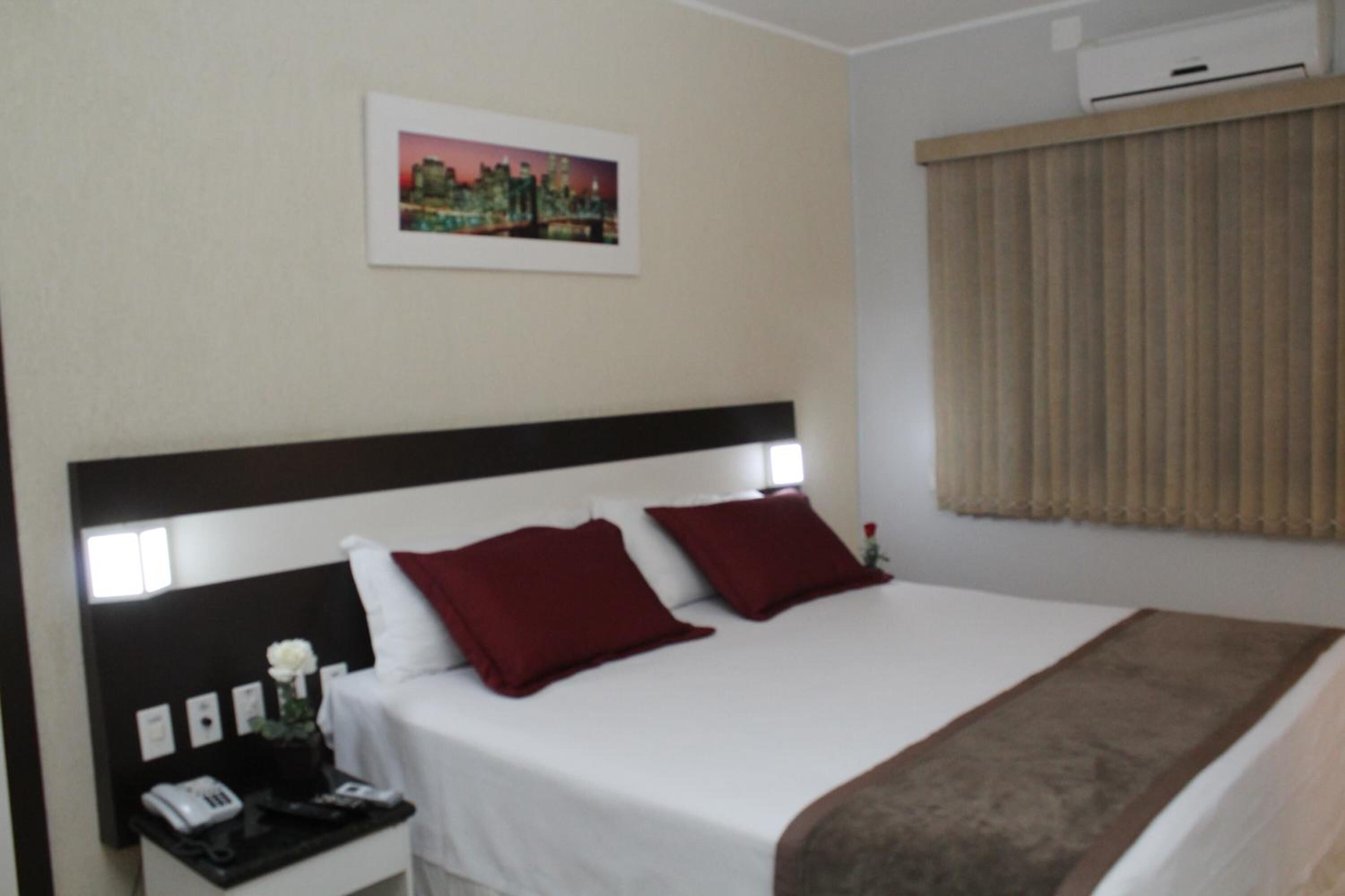A hotel room with a large bed, a nightstand with a phone, and a picture on the wall.