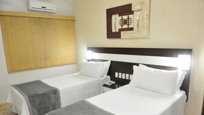 Two single beds with white linens and gray throw blankets, a bedside table with a phone, and a wall-mounted air conditioner. - Itamaraty Hotel (Anapolis)