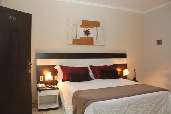 A hotel room with a bed, bedside tables, lamps, and a wall-mounted artwork.