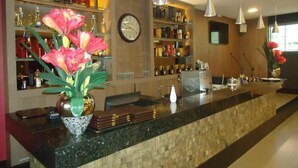 A hotel bar with a long counter, shelves with bottles, a clock, and hanging pendant lights. - Itamaraty Hotel (Anapolis)