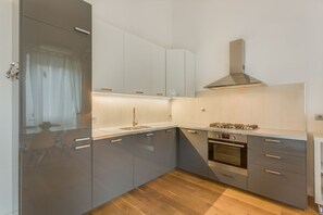 A modern kitchen with grey cabinets, a stainless steel range hood, and a built-in oven. - Apartments Florence - Fortezza (Firenze)