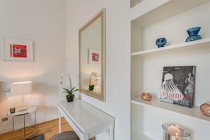 A modern room with a white console table, a large mirror, a potted orchid, and a shelf with decorative items. - Apartments Florence - Fortezza (Firenze)
