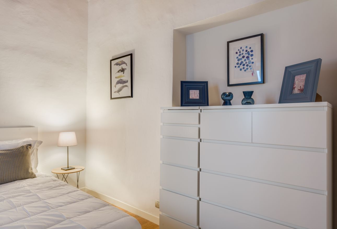 A bedroom with a bed, a bedside table with a lamp, a dresser, and wall art.
