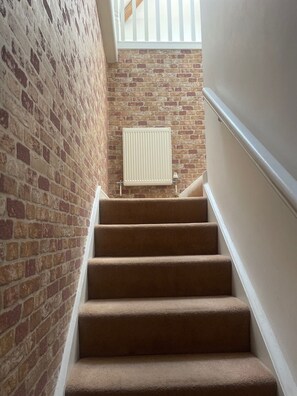 A staircase with carpeted steps leading to a landing with a radiator. - Beach House - Penthouse 3 Bed Apartment (Southport)