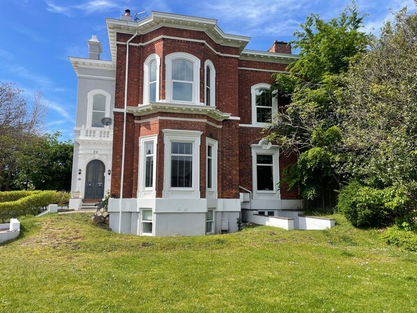 A large, two-story brick house with white trim and multiple windows, surrounded by a well-maintained lawn and trees. - Beach House - Penthouse 3 Bed Apartment (Southport)