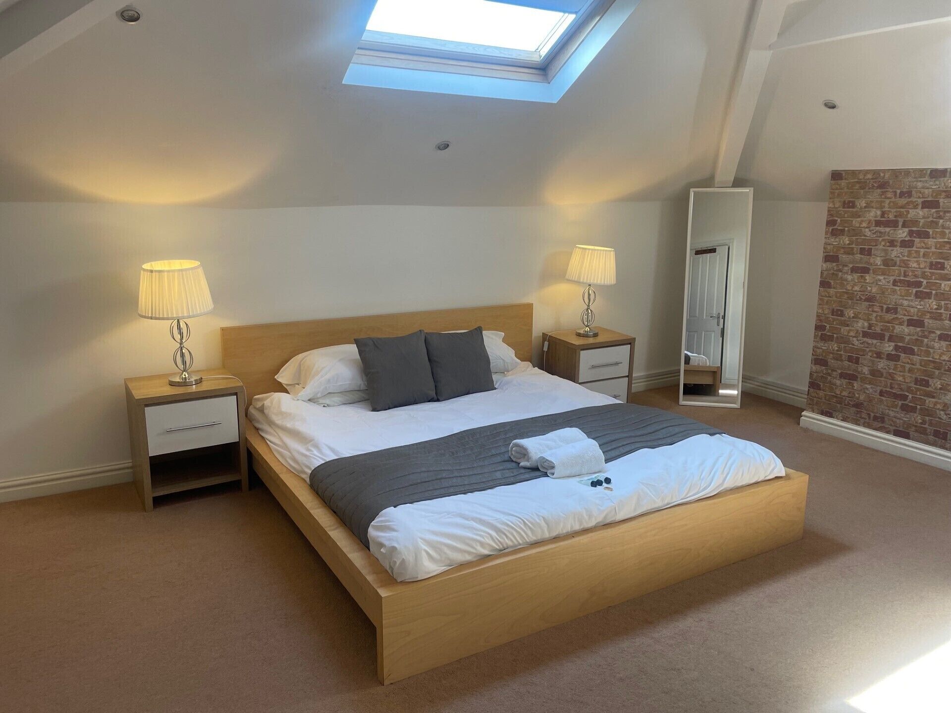 A bedroom with a skylight, a bed with pillows, nightstands, and a mirror.
