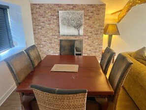 A dining area with a brick wall, a painting of a tree, and a table with chairs. - Beach House - Penthouse 3 Bed Apartment (Southport)