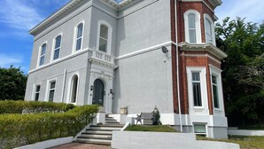 A two-story building with a symmetrical facade, a central entrance with steps, and a small garden area with a bench. - Beach House - Penthouse 3 Bed Apartment (Southport)