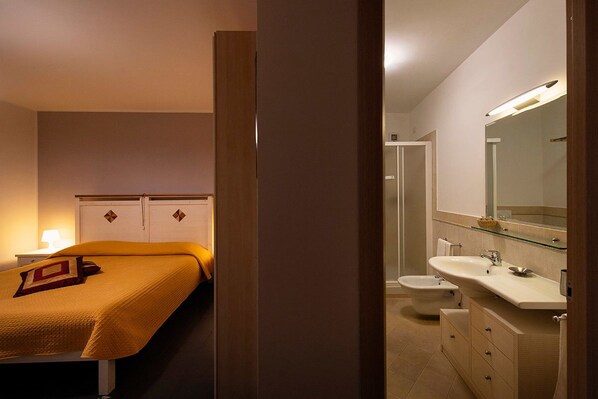 A hotel room with a bed, bedside table, and a bathroom with a sink, mirror, and toilet. - B&B La Piazzetta (Orvieto)