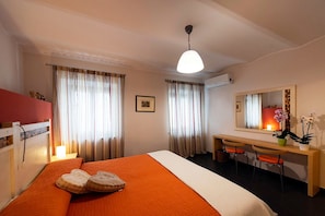 A hotel room with a bed, a desk, two chairs, a mirror, and a potted plant.