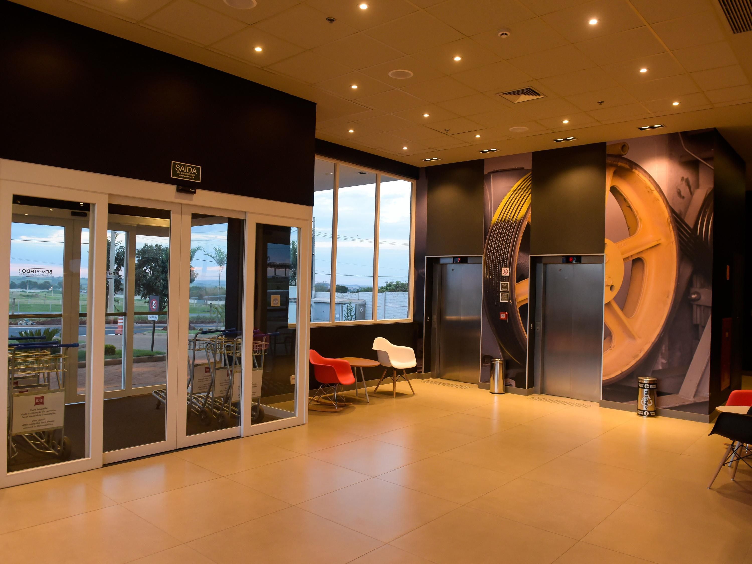 Um hall de hotel moderno com entrada por porta de vidro, vista para o exterior e um grande mural na parede.