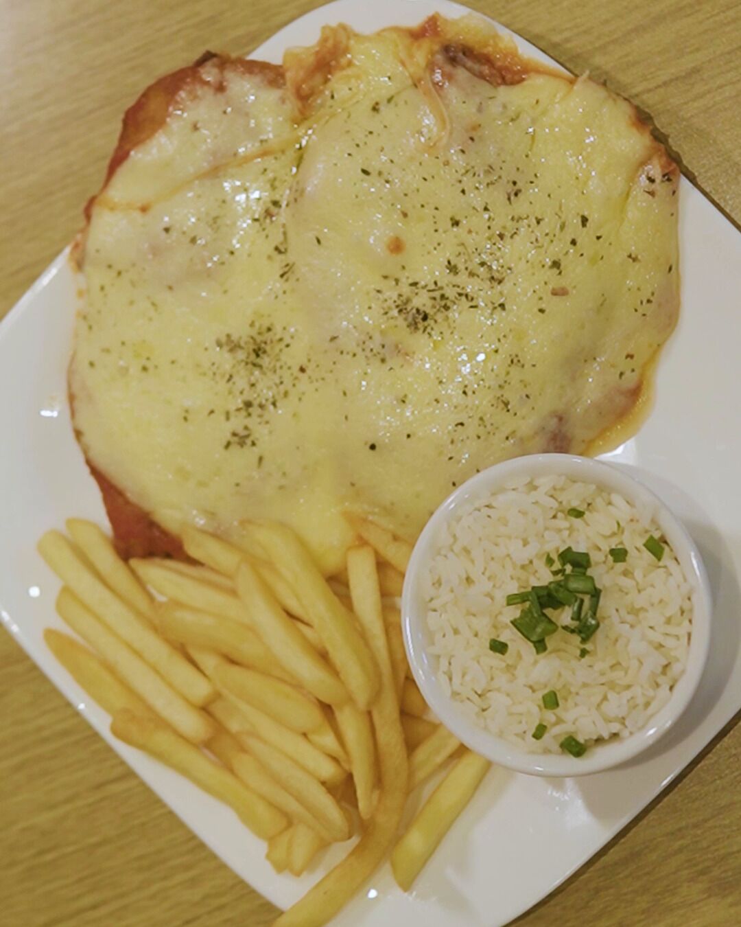 Un piatto con un filetto di pesce ricoperto di formaggio, patatine fritte e una piccola ciotola di riso.