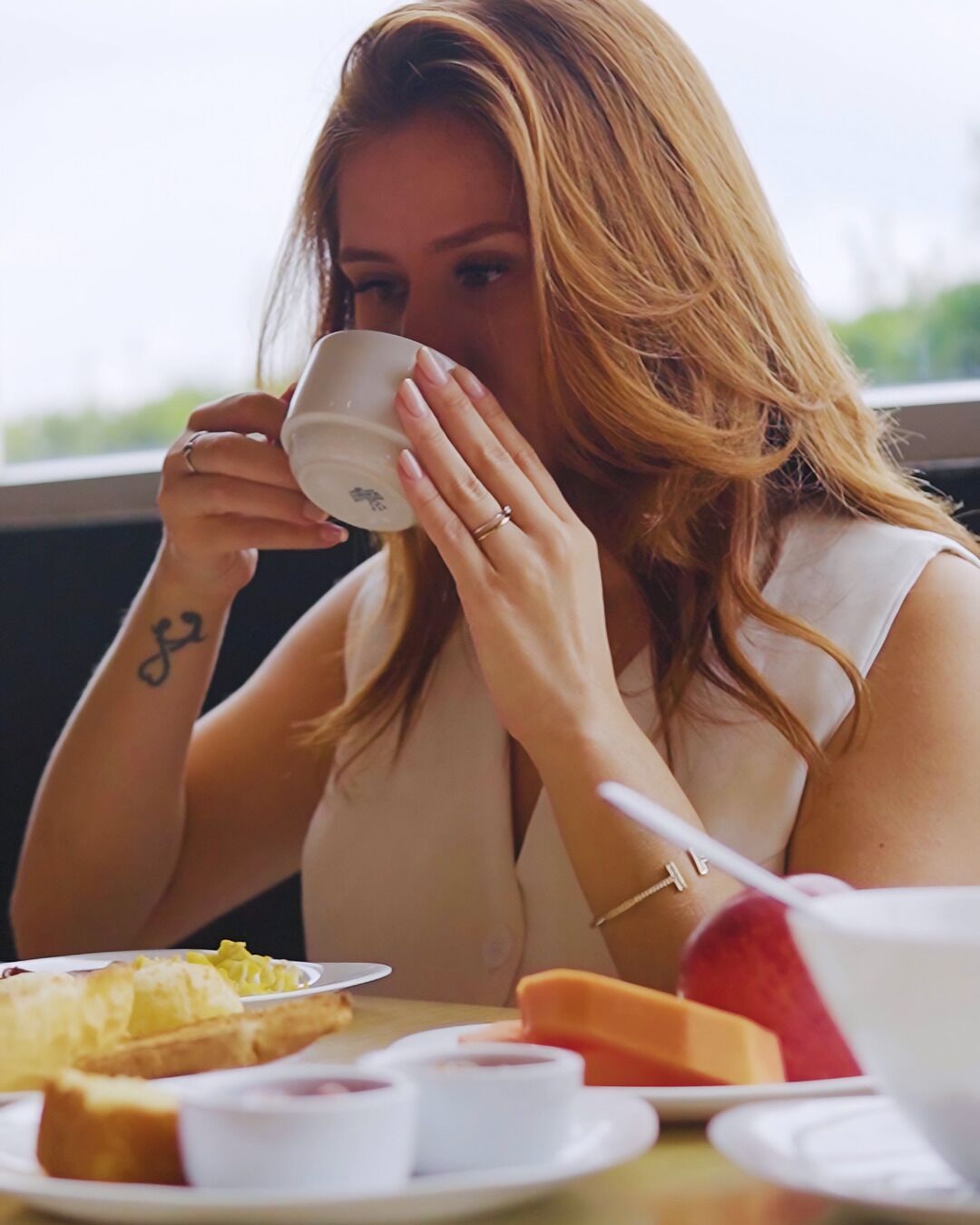 Une personne est assise à une table devant une tasse, une assiette contenant de la nourriture et un bol.