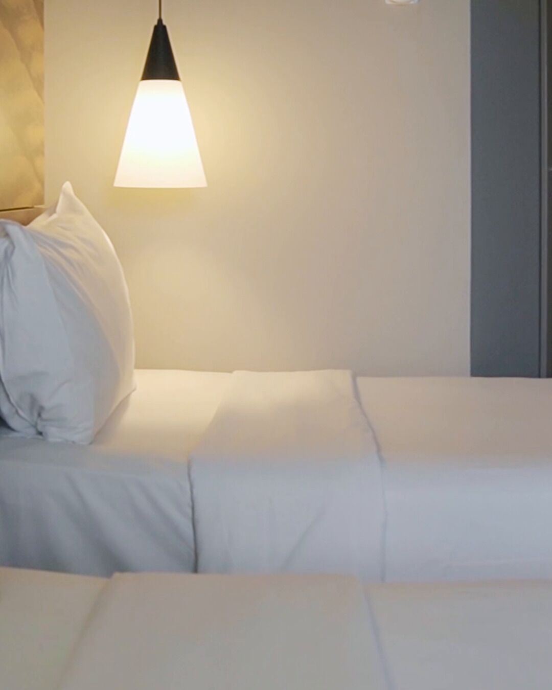 A bed with white bedding, a pillow, and a hanging light fixture.