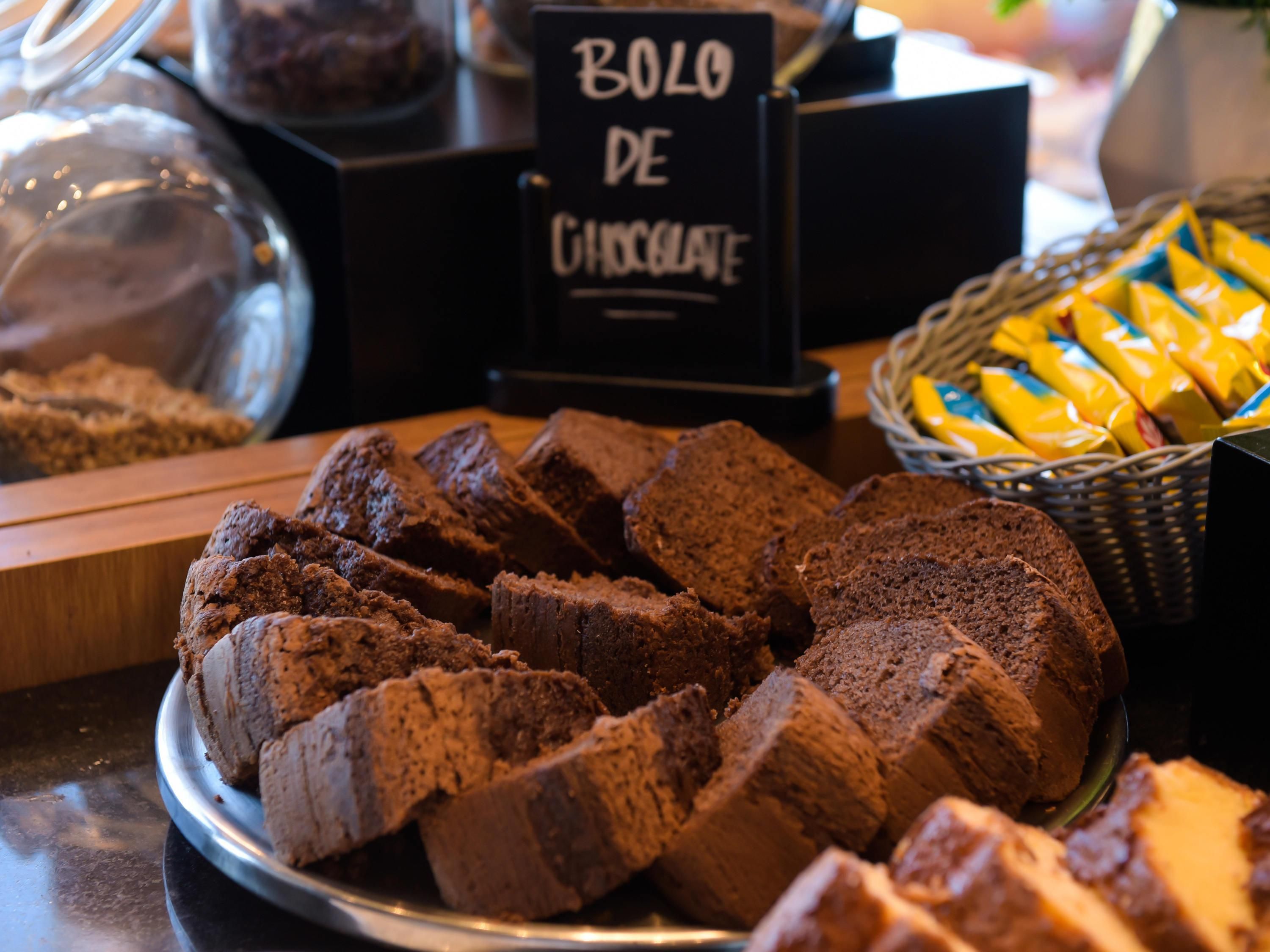 A display of sliced chocolate bread on a metal plate, with a sign reading 'Bolo de Chocolate' in the background.