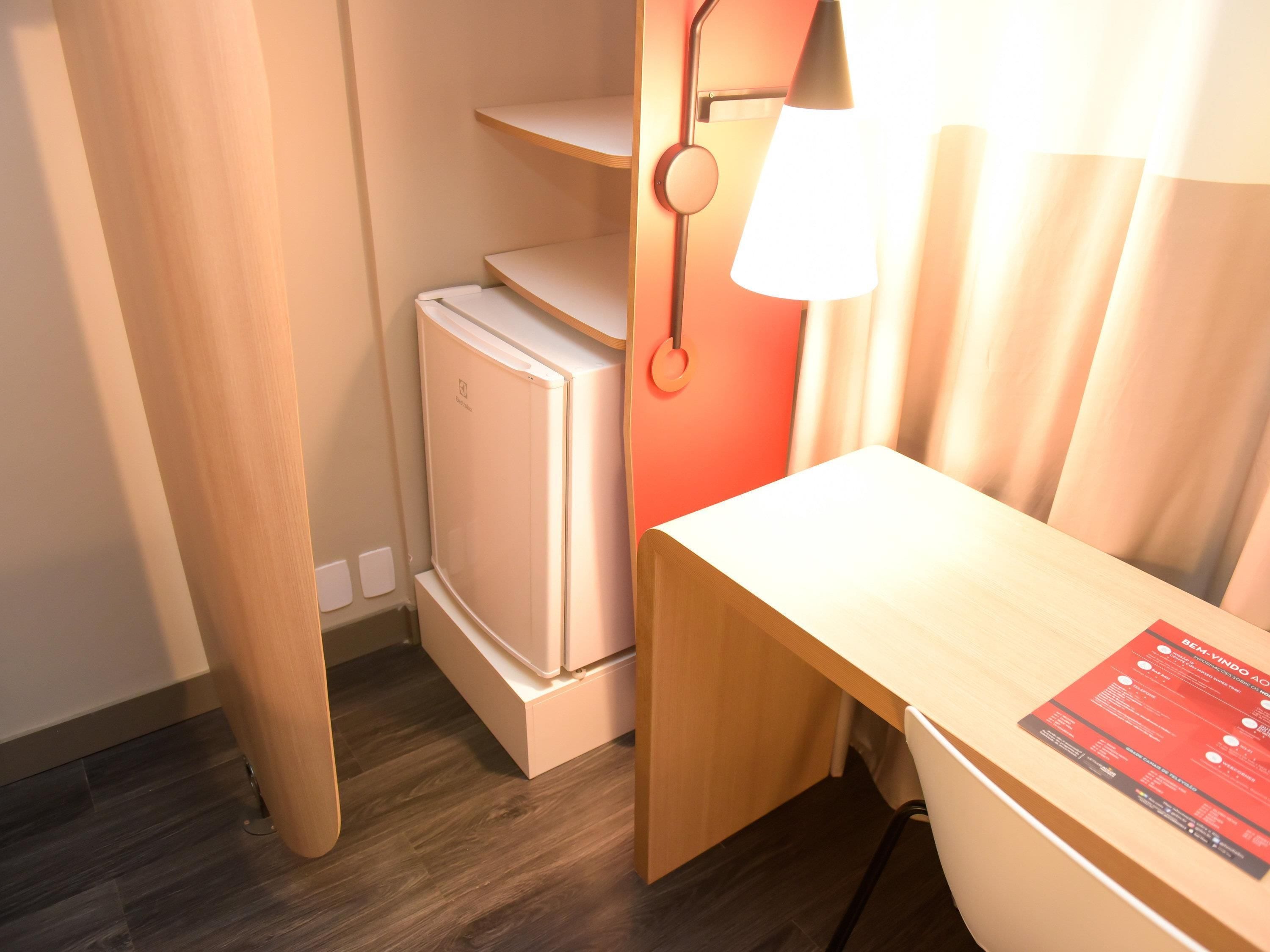 A compact room with a desk, a small refrigerator, and a lamp.