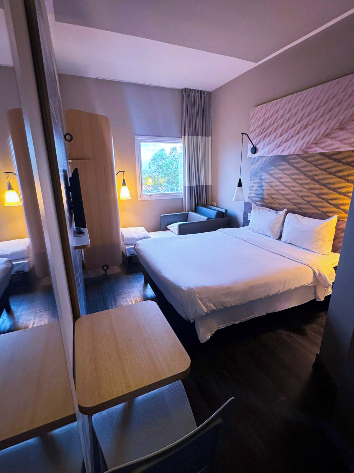 Een moderne hotelkamer met een groot bed, nachtkastjes, een bureau en een raam met gordijnen.