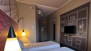 Une chambre d’hôtel avec deux lits, un téléviseur fixé au mur et un ventilateur de plafond.