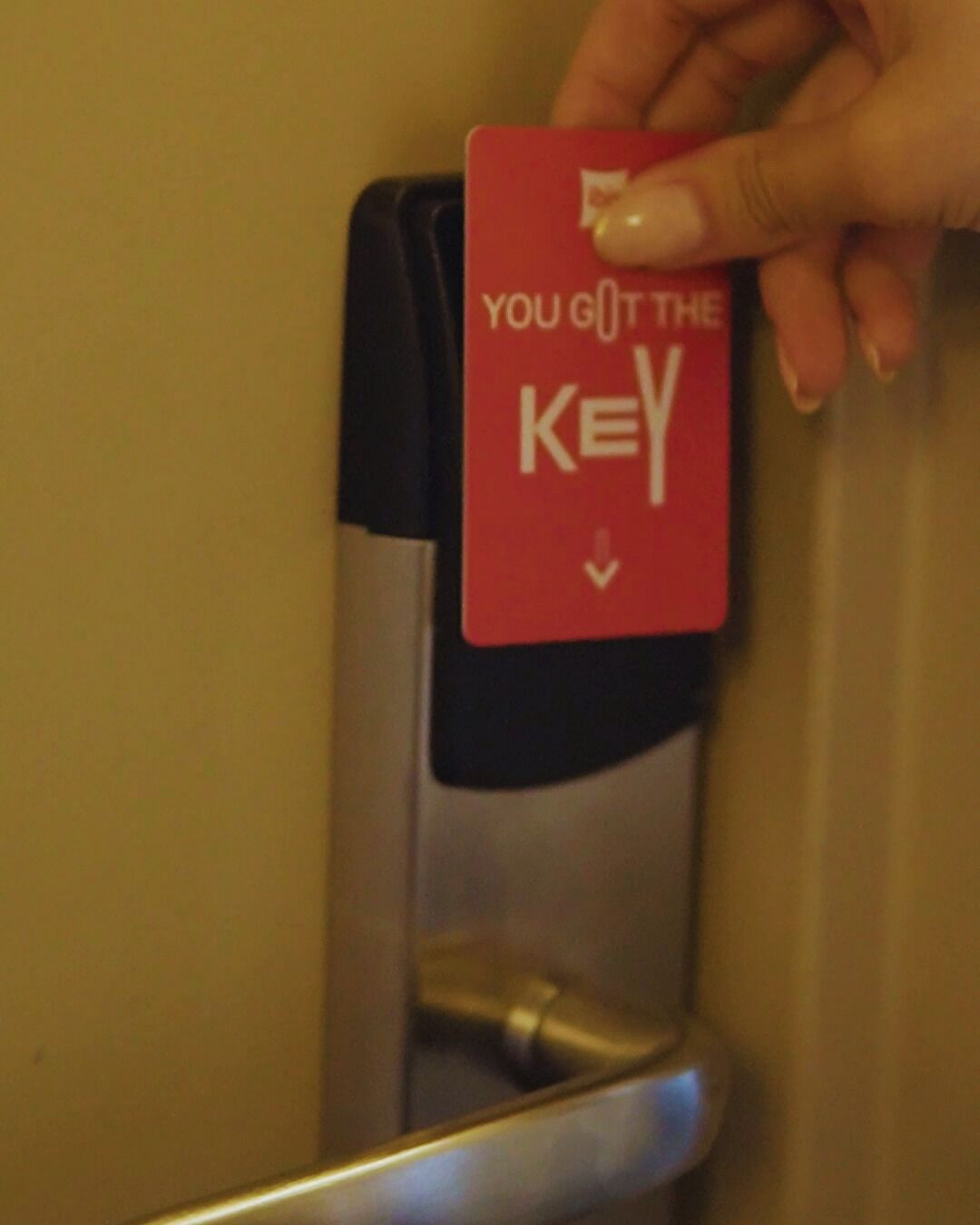 A hand holding a red card with the text 'YOU GOT THE KEY' near a door lock.