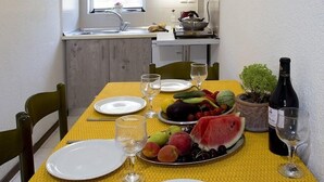 Comedor con mantel amarillo, platos blancos, cubiertos, una botella de vino y una bandeja de frutas.