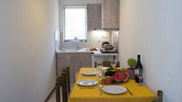 A compact dining area with a yellow tablecloth, wooden chairs, and a window overlooking the kitchen.