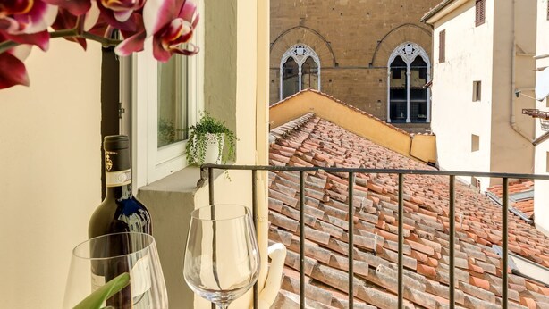 Un balcón con vistas a un patio interior, un edificio con ventanas de arco y una botella de vino.