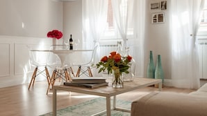 Una sala de estar moderna con comedor, sillas traslúcidas, una mesa de centro de madera y un jarrón con flores.