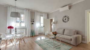 Una sala de estar moderna con una mesa de comedor de vidrio, un sofá color beige y un reloj en la pared.