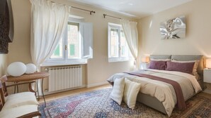 Un dormitorio con cama, mesita de noche, silla, ventana con cortinas y radiador.