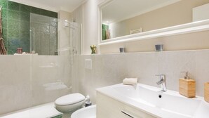 Un baño moderno con cabina de ducha de vidrio, bañera, lavamanos e inodoro.