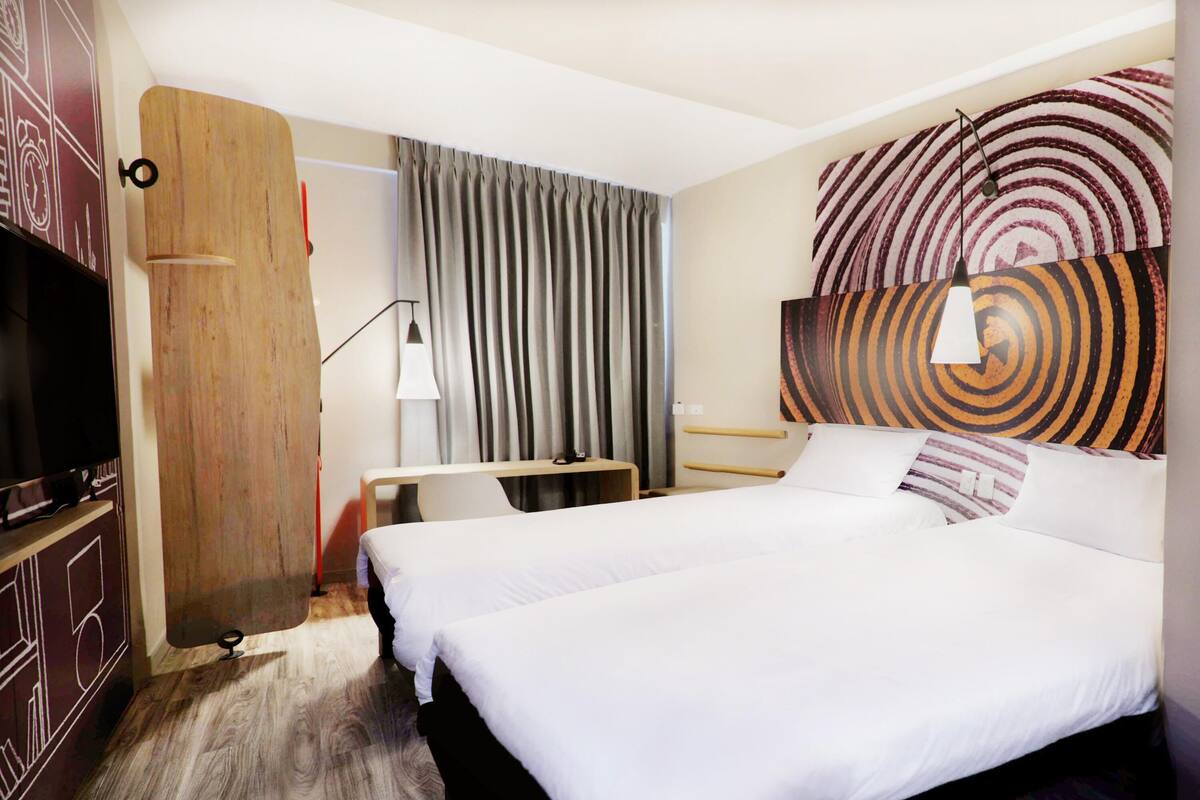 Habitación de hotel con dos camas, un escritorio, un televisor y un cuadro abstracto grande en la pared.