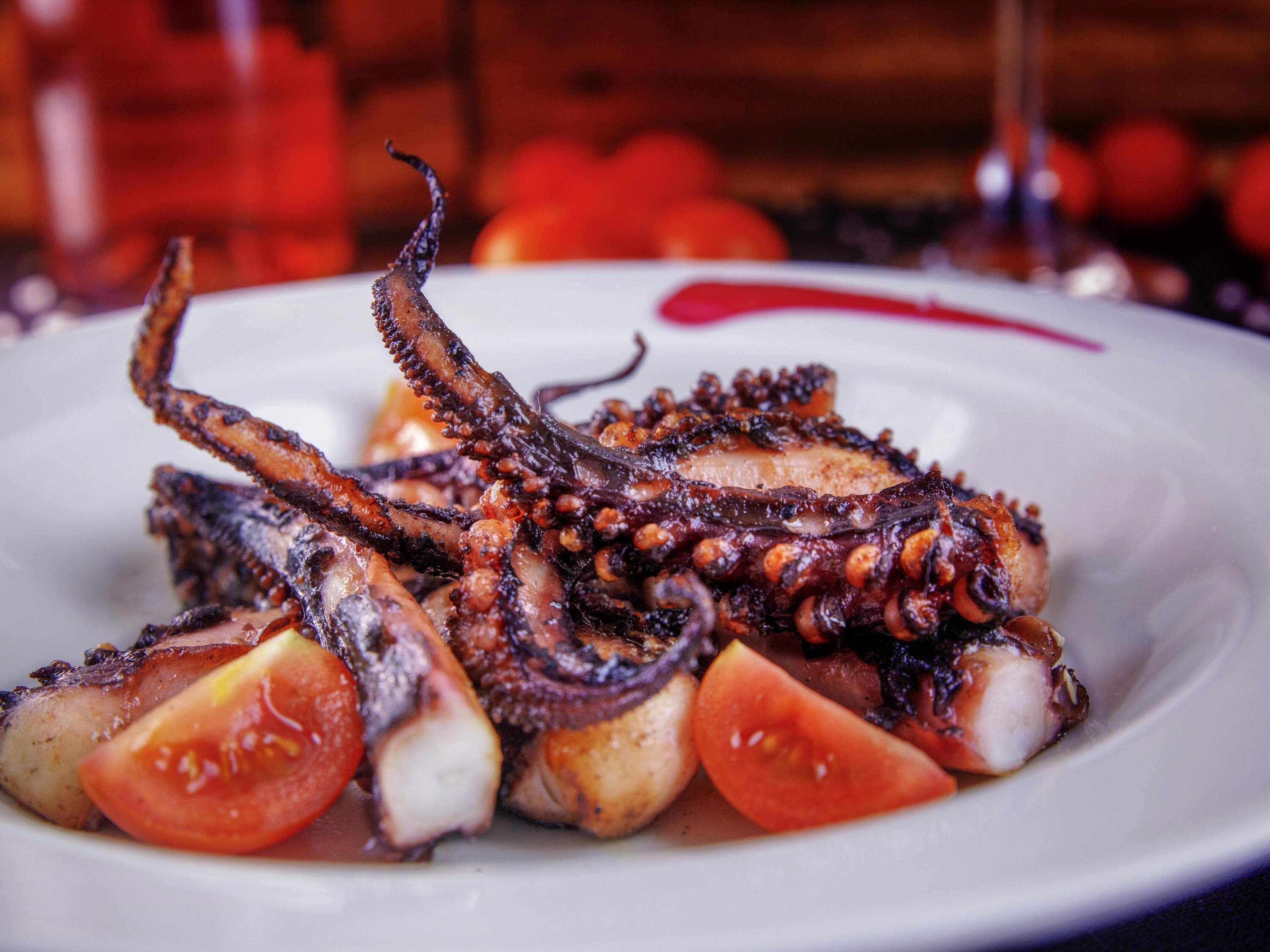 A plate of grilled octopus with lemon slices and tomato wedges.