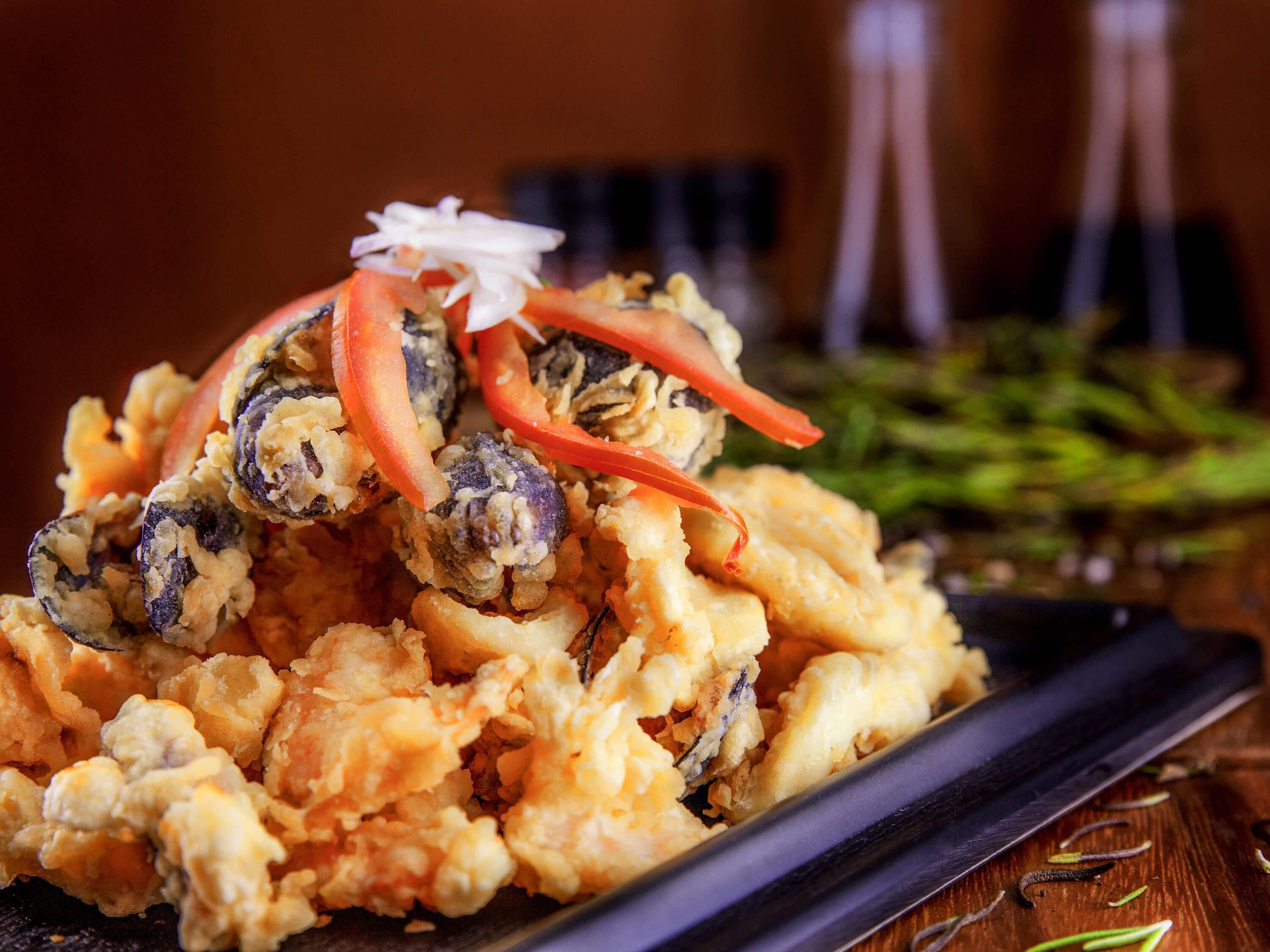 Un piatto di pesce fritto guarnito con peperoncino rosso e cipolla bianca.