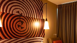 A hotel room with a large circular wall art, two wall-mounted lamps, a bed with pillows, a chair, and a curtain. - ibis Apartado (Apartadó)
