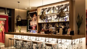 A bar area with a counter, stools, hanging lights, and a wall with a leaf pattern. - ibis Apartado (Apartadó)