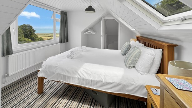 A bedroom with a large bed, a wooden headboard, a bedside table, and a view of the outdoors through a skylight. - West Wind Holiday Home in Porlock (Porlock)