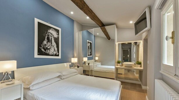 A modern bedroom with a large bed, bedside tables, a mirror, a TV, and a bathroom visible through an open door.