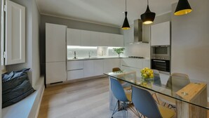 A modern kitchen with white cabinets, a glass dining table, and two blue chairs.