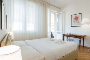 Une chambre d’hôtel avec un lit, un bureau, une chaise, une lampe et un tableau encadré au mur.
