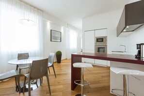 A modern kitchen with a central island, a dining area with a glass table, and a view of the city.