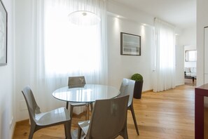 Un espace repas moderne avec une table ronde en verre et quatre chaises, une plante en pot et un tableau encadré au mur.