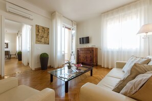 Un salon avec une table basse en verre, un canapé, un meuble en bois, un téléviseur et un tableau accroché au mur.