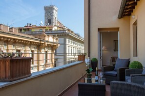 A balcony with wicker furniture, a potted plant, and a view of historic buildings. - Apartments Florence - Repubblica Terrace (Firenze)