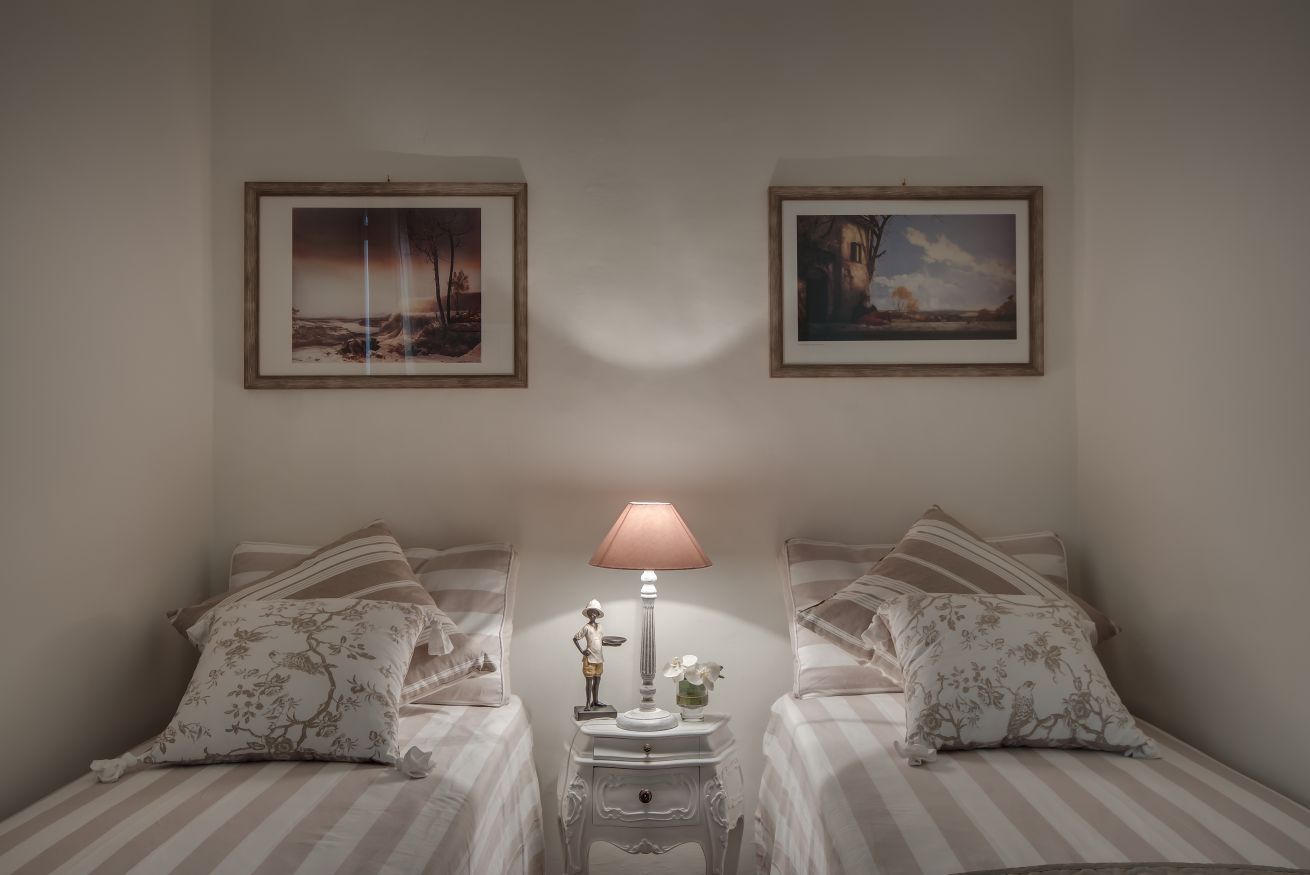 Un dormitorio con dos camas, una mesita de noche con lámpara y dos cuadros en la pared.