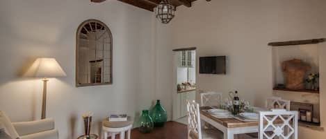 A dining area with a wooden table set for four, white chairs, a lamp, and a mirror on the wall.