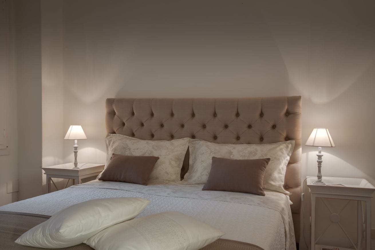 A bedroom with a tufted headboard, two bedside tables with lamps, and a bed with pillows.