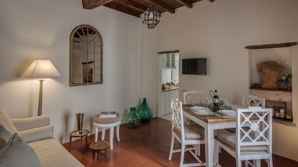 Un coin repas avec une table en bois dressée pour quatre personnes, des chaises blanches, une lampe et un miroir au mur.
