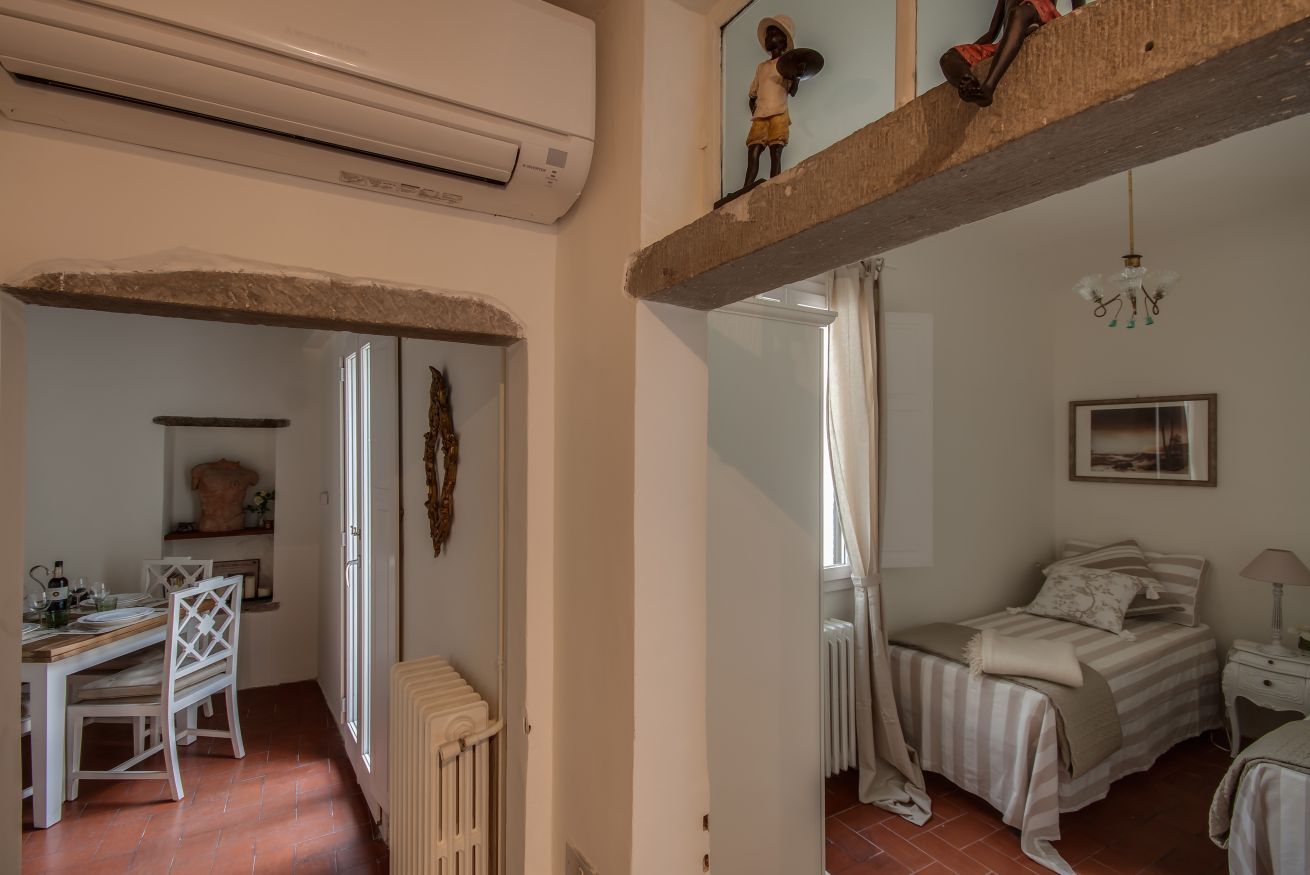 Een kamer met een bed, een bureau en een stoel. Er is een radiator, een raam en een hanglamp.