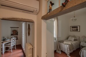 Une pièce comprenant un lit, un bureau et une chaise. On y trouve également un radiateur, une fenêtre et un luminaire suspendu.